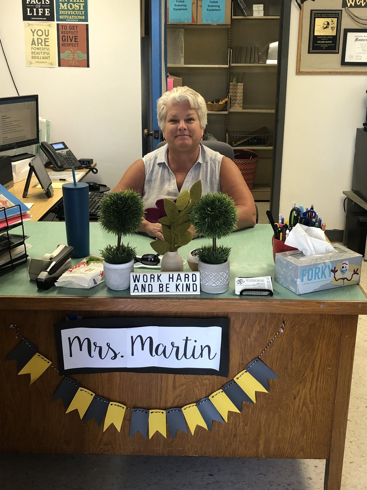 Colleen Martin at her College and Career Center desk beneath a sign reading Work Hard and Be Kind